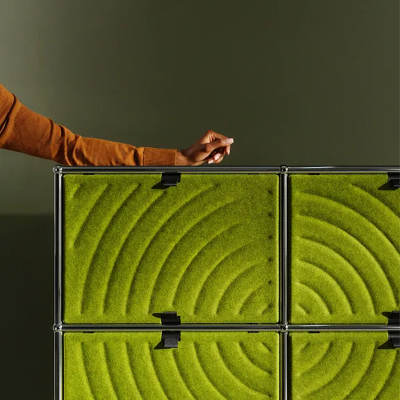 USM Haller Regal mit 4 USM Haller Soft Panels in Grün. Am Rand des Bildes sieht man einen Arm, der auf dem Möbel liegt.